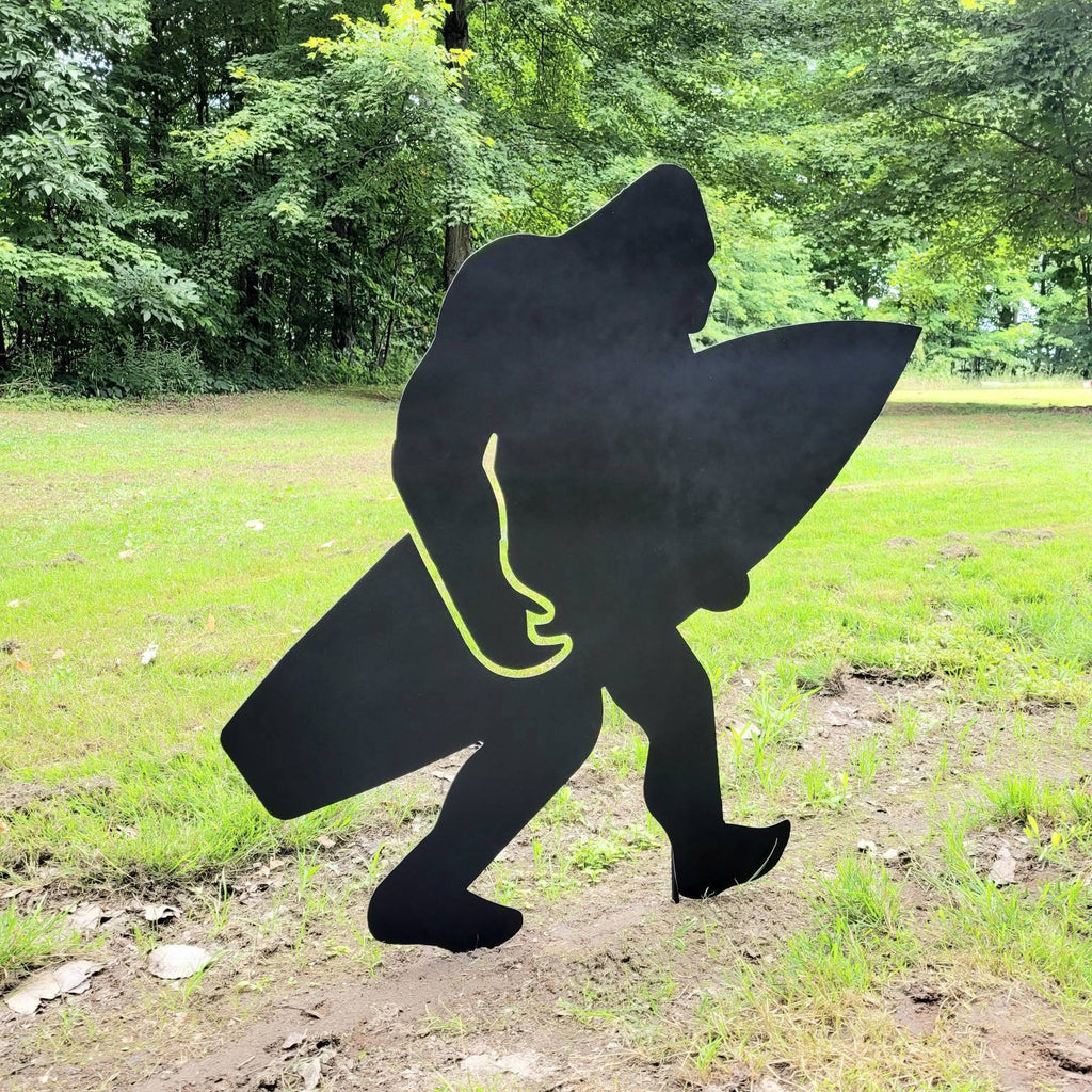 Surfing Bigfoot Metal Yard Stake Metal Garden Stake — shown on a rustic wall