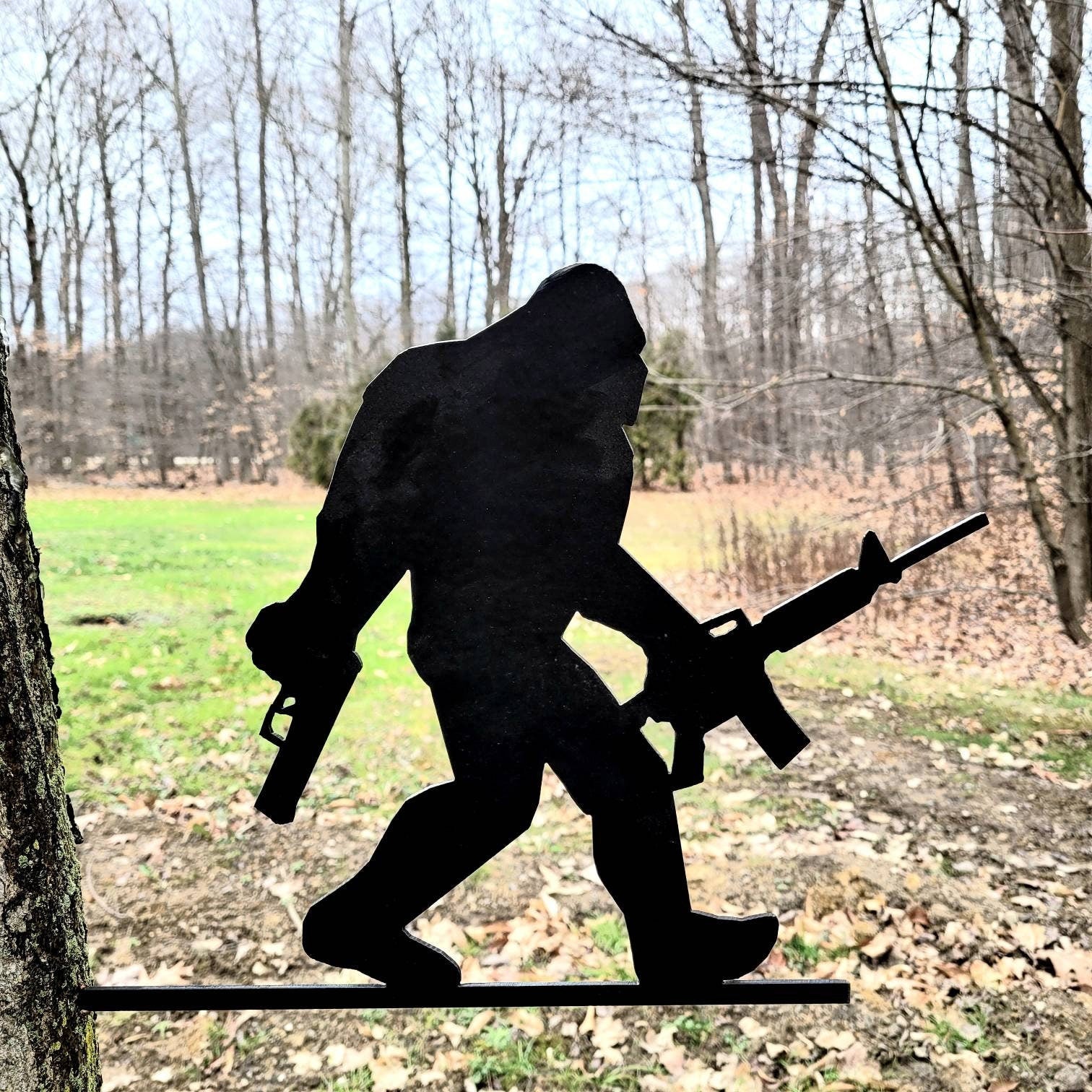 Armed Bigfoot Metal Garden Stake Metal Garden Stake — shown on a rustic wall