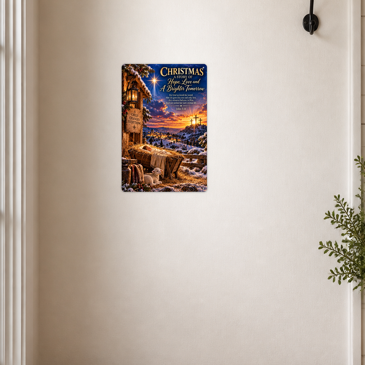 The aluminum sign showing a nativity manger scene with the star of Bethlehem and three crosses on a distant hill, mounted on a cream wall near a coat hook and a potted plant.
