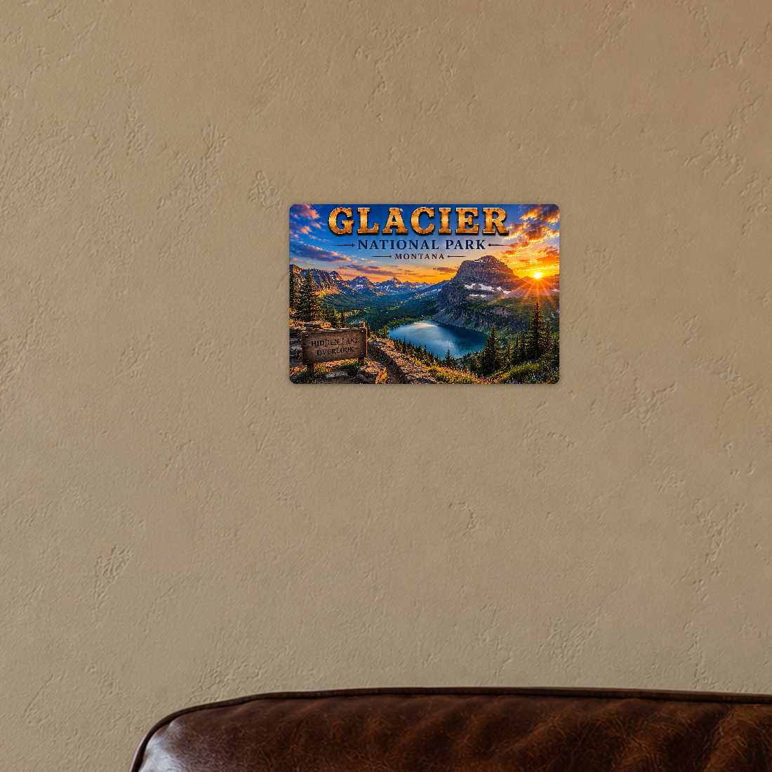 Sign showing Glacier Hidden Lake Overlook lettering and a sunset mountain lake, displayed on a warm tan plaster wall above the corner of a brown leather chair.