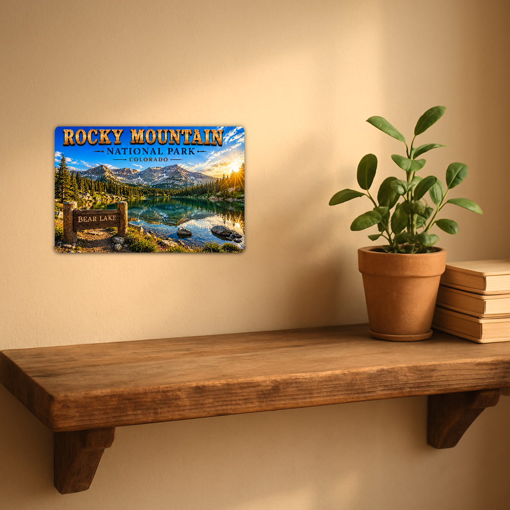 Sign showing Rocky Mountain Bear Lake lettering and a turquoise lake below snowy mountains, displayed on a warm beige wall above a rustic shelf with a potted plant and books.