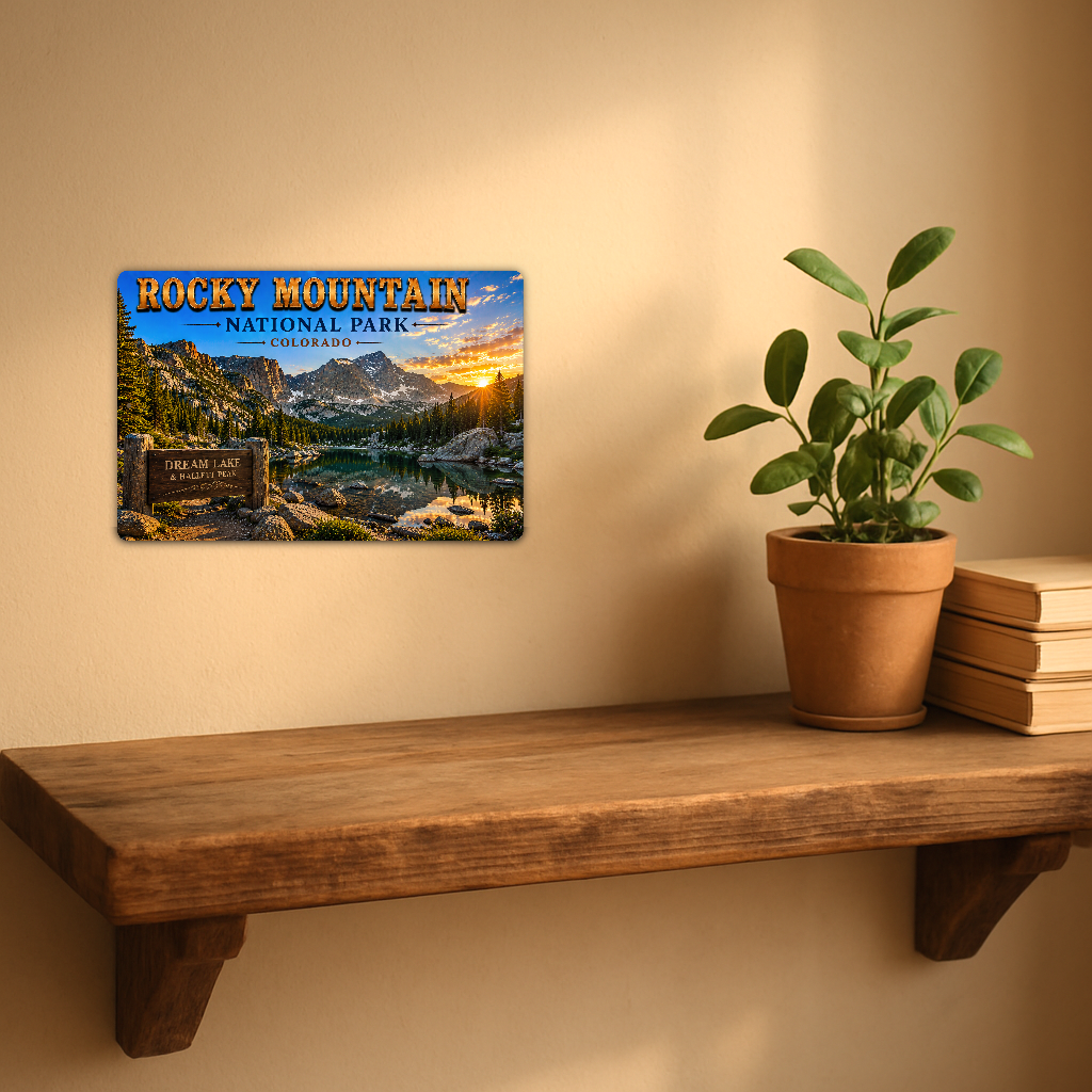 Sign showing Rocky Mountain Dream Lake Hallett Peak lettering with a mountain lake and pine forest, displayed on a warm beige wall above a rustic shelf with a potted plant and books.