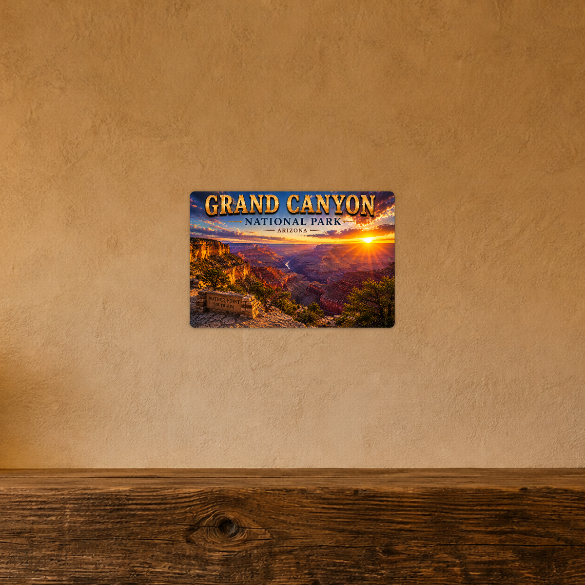 Sign showing Grand Canyon Mather Point lettering and layered canyon walls at sunset, displayed on a warm tan textured wall above a wooden ledge.