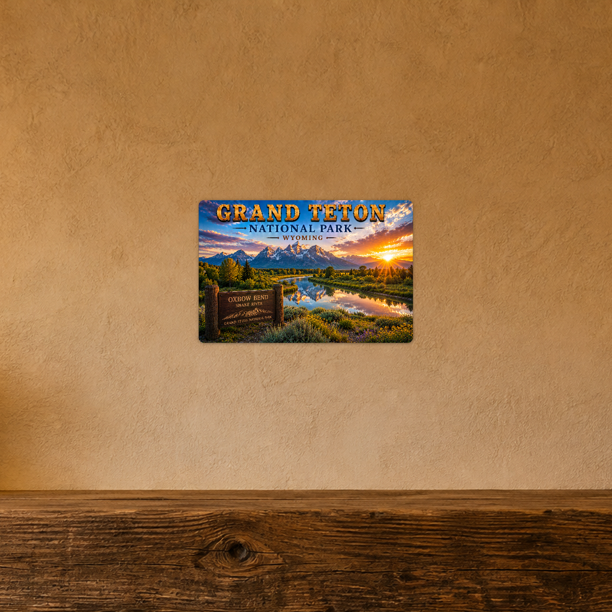 Sign showing Grand Teton Oxbow Bend Snake River lettering with mountains reflected in a forest river, displayed on a warm tan textured wall above a wooden ledge.
