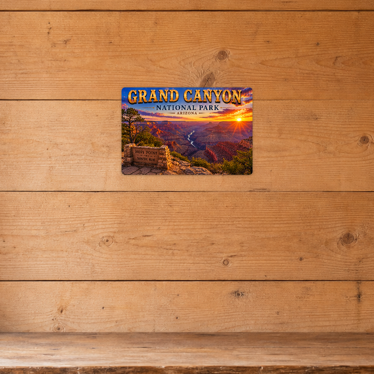 Sign showing Grand Canyon Hopi Point South Rim lettering and canyon river bends at sunset, displayed on a honey-colored horizontal wood-plank wall.