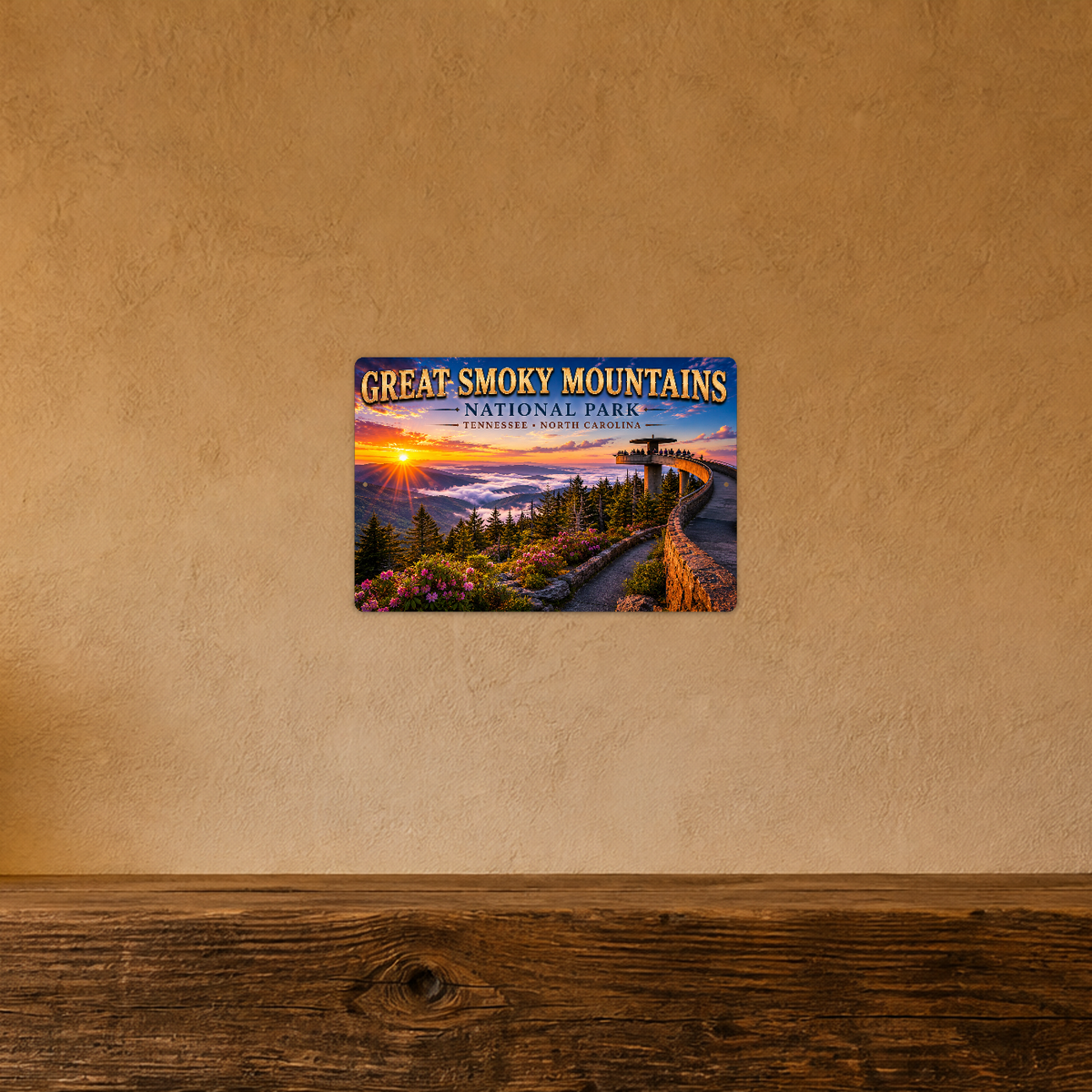 Sign showing Great Smoky Mountains lettering and a curved observation walkway above clouds and fir trees, displayed on a warm tan textured wall above a wooden ledge.