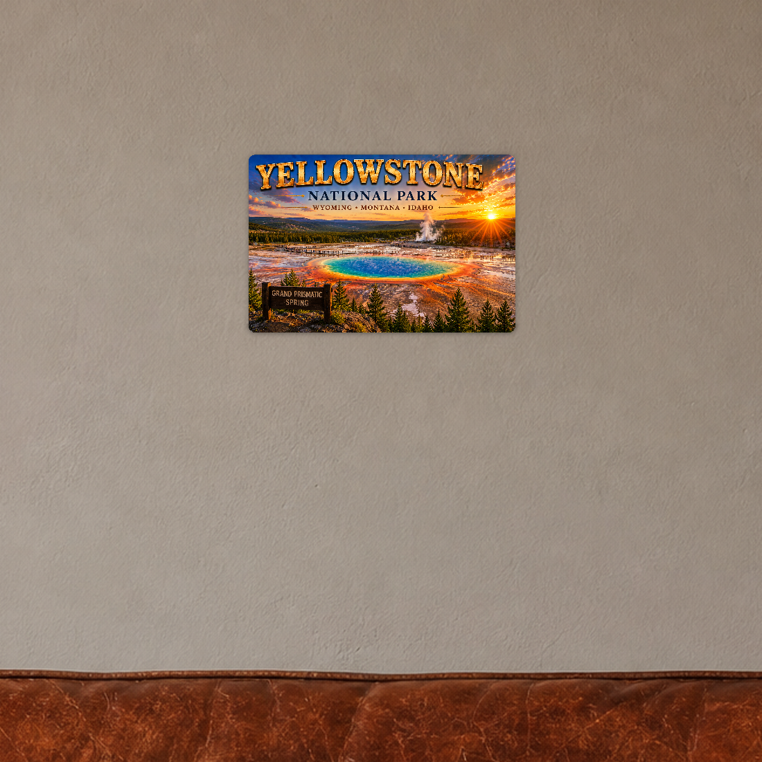Sign showing Yellowstone Grand Prismatic lettering and a rainbow-colored hot spring, displayed on a pale cream plaster wall above a chair corner.