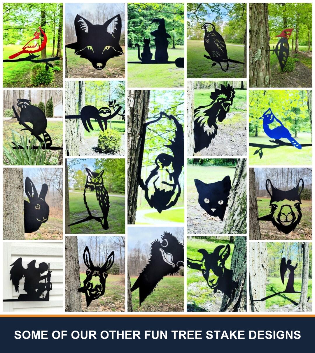 A sampler grid of other TKG metal tree and garden stake designs, shown staked in flower beds and mounted on trees, posts and mailboxes. Captioned “some of our other fun tree stake designs” — these are other designs we make, not what is included with this listing.