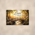Wooden footbridge at sunrise memorial art titled "Love Never Ends" on a 12x8 inch sublimated aluminum sign with rounded corners and mounting holes, shown straight on against a warm neutral wall