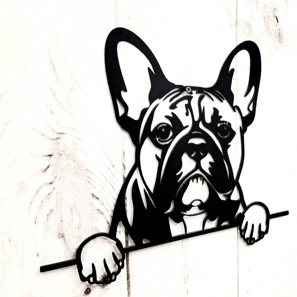 Angled close view of a black dog face cutout with upright ears and paws against white wooden boards.