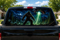 Bigfoot UFO Abduction perforated rear-window decal installed on a pickup truck back glass, showing a sasquatch in a moonlit forest as a UFO beams a hiker up in a green tractor beam