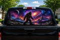 Bigfoot Galaxy Walker perforated rear-window decal installed on a pickup truck back glass, showing a sasquatch walking under a spiral galaxy, planets and a purple cosmic sky