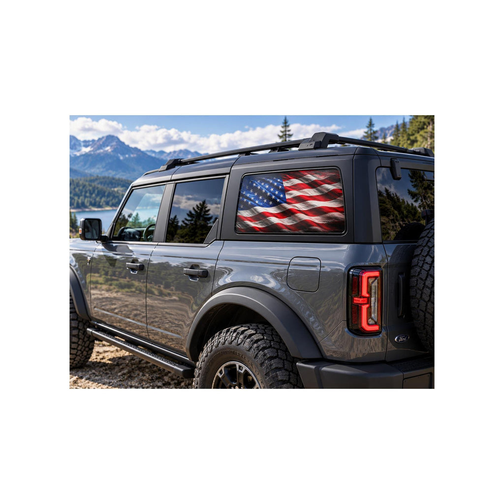 Ford Bronco rear side window with a perforated decal of a full-color, weathered American flag waving against a plain black background, applied to the outside of the glass.