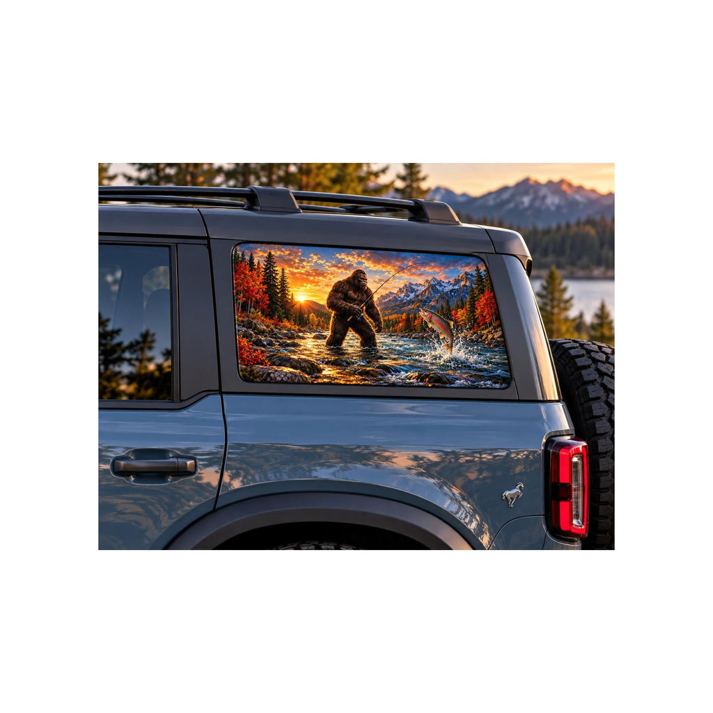 Ford Bronco rear side window with a perforated decal of Bigfoot fly-fishing in a mountain river at sunset, a trout jumping from the water, applied to the outside of the glass.