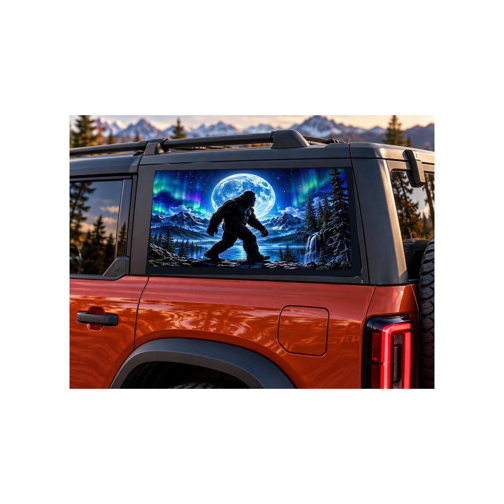 Ford Bronco rear side window with a perforated decal of Bigfoot walking beside a mountain lake under a full moon and green and purple northern lights, applied to the outside of the glass.