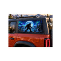 Ford Bronco rear side window with a perforated decal of Bigfoot walking beside a mountain lake under a full moon and green and purple northern lights, applied to the outside of the glass.