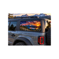 Ford Bronco rear side window with a perforated decal of a waving American flag over a snow-capped mountain range and a calm lake at sunset, applied to the outside of the glass.