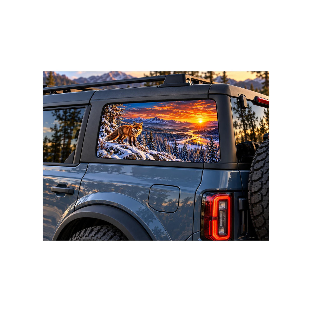 Ford Bronco rear side window with a perforated decal of a red fox standing on a snowy ridge above a winding river valley at sunset, snow-capped mountains in the background, applied to the outside of the glass.