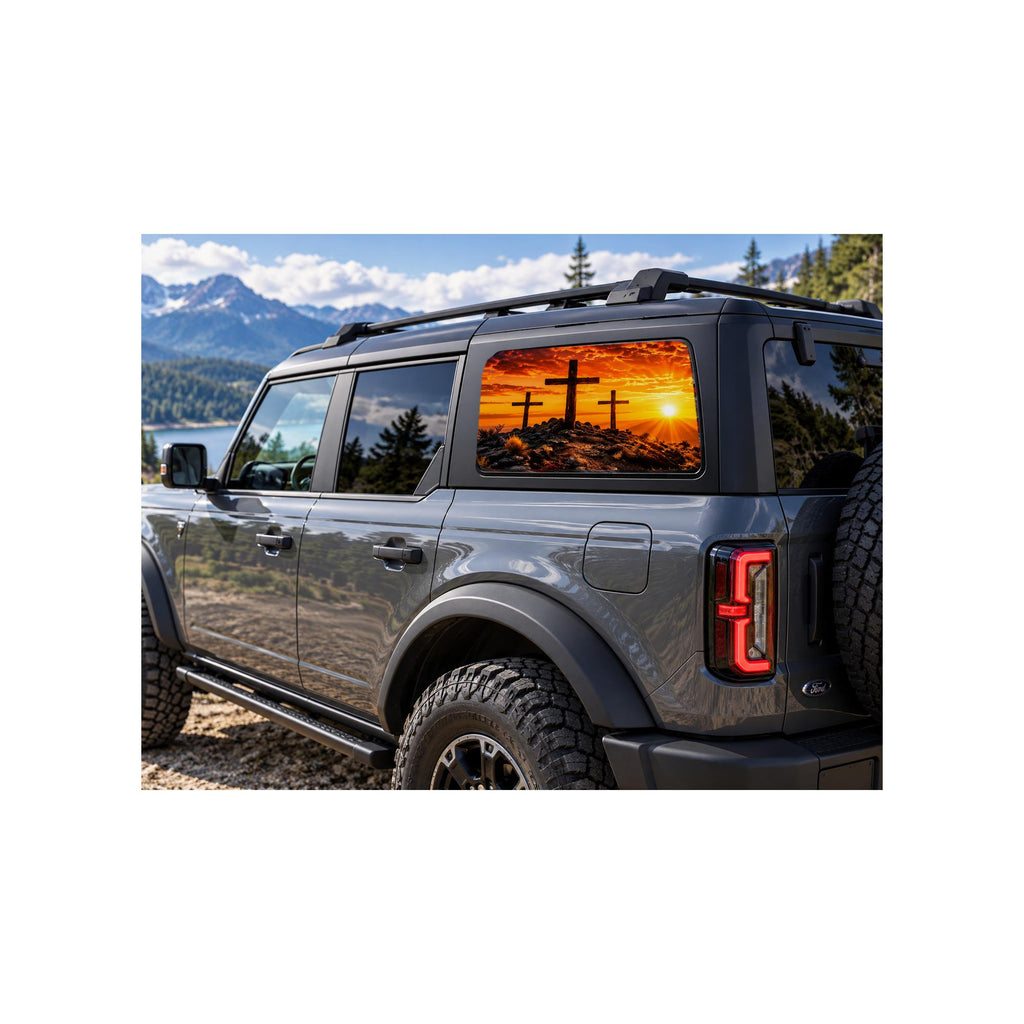 Ford Bronco rear side window with a perforated decal of three wooden crosses silhouetted on a hill at a fiery orange sunset, applied to the outside of the glass.