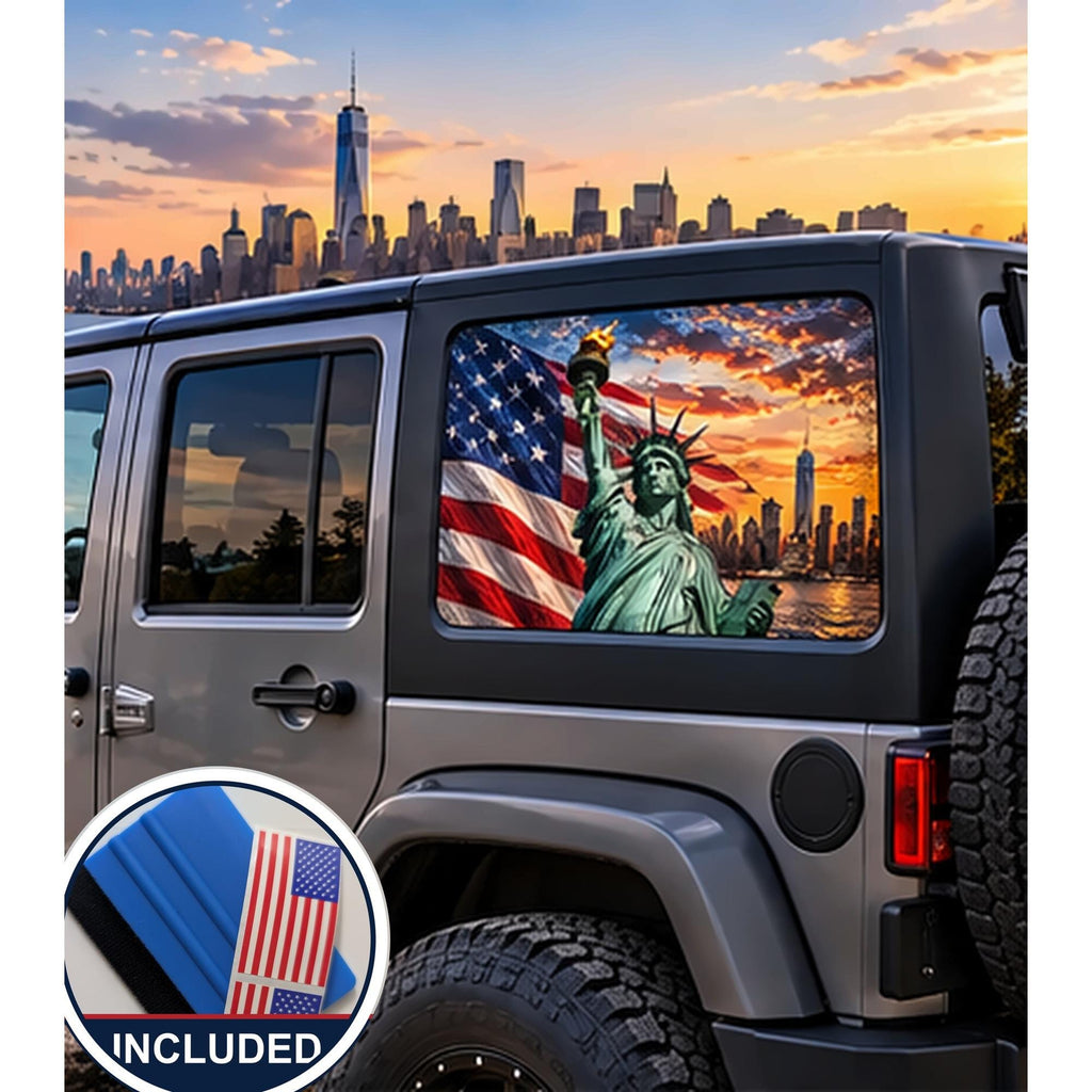 Jeep Wrangler 4-door rear quarter window with a perforated decal of the Statue of Liberty holding her torch in front of a waving American flag and the New York City skyline at sunset, applied to the outside of the glass. An INCLUDED badge in the corner shows the felt squeegee and 2 American flag decals that come with every set.
